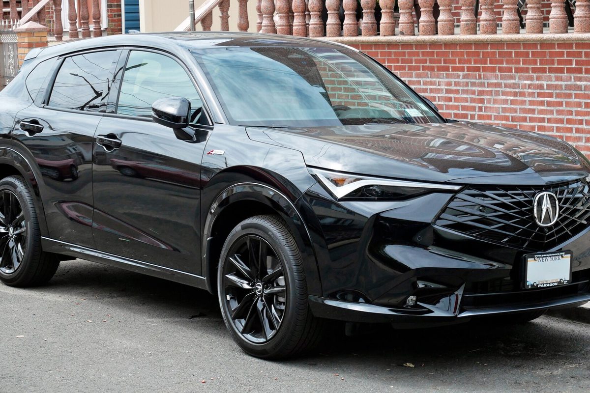 A black Acura ADX crossover with black wheels, parked at a curb in front of a red brick wall