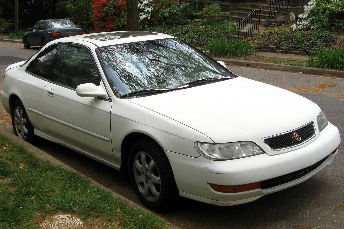 A white 1998-1999 Acura CL coupe with a sunroof, parked at a curb beside a grass strip on a residential street