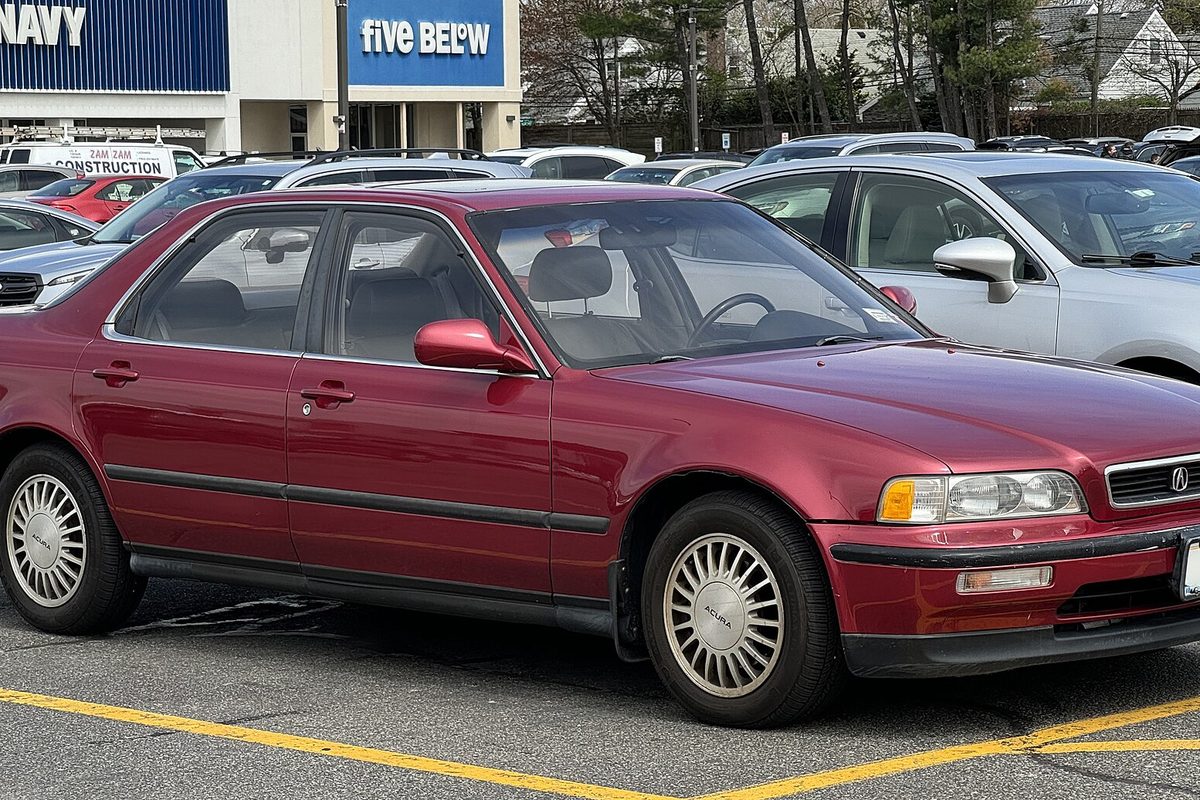 A dark red 1992 Acura Legend L sedan with lattice-style wheels, parked in a shopping-center lot