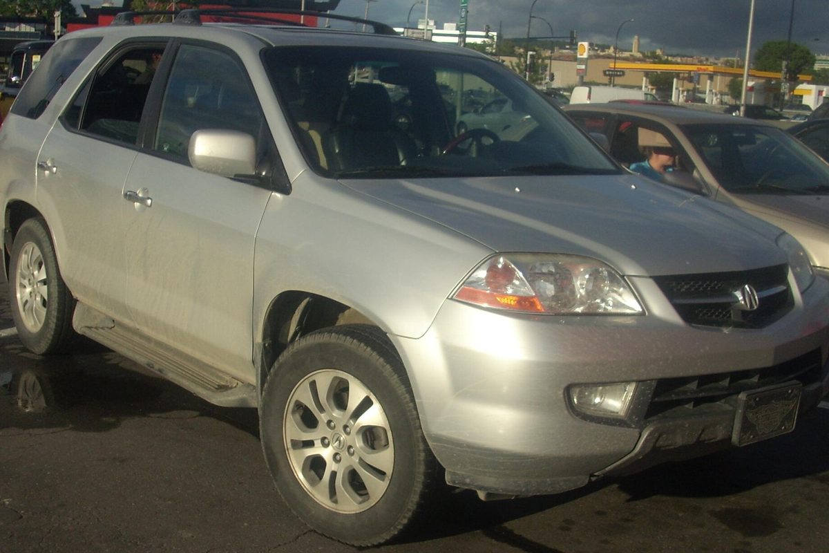 A silver first-generation Acura MDX SUV parked on wet pavement in a busy parking lot