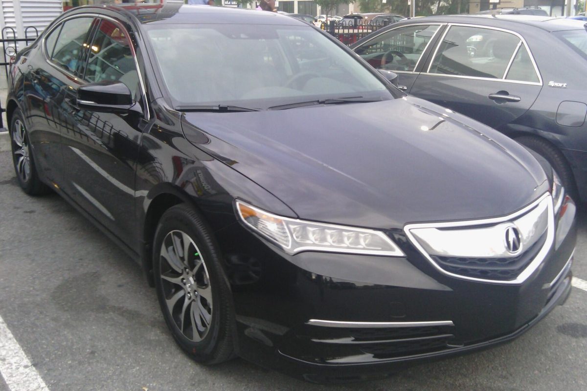 A black first-generation Acura TLX sedan parked at a curb on a city street, with another car beside it