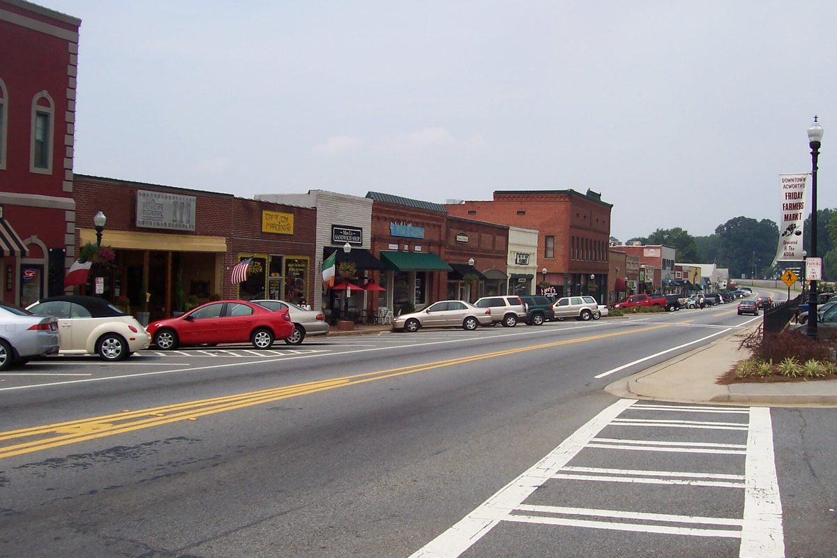 Main Street in historic downtown Acworth, with brick storefronts and awnings on the left and cars parked along the curb