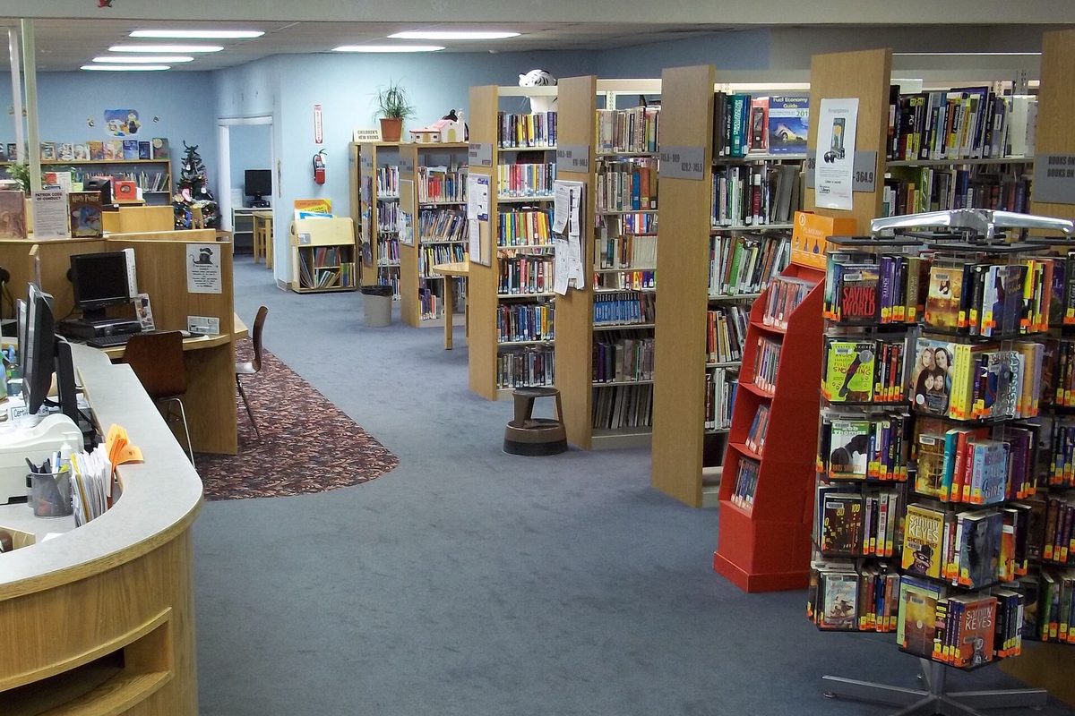 Inside the Adelanto Branch Library: rows of wooden bookshelves, a red paperback rack and the front desk