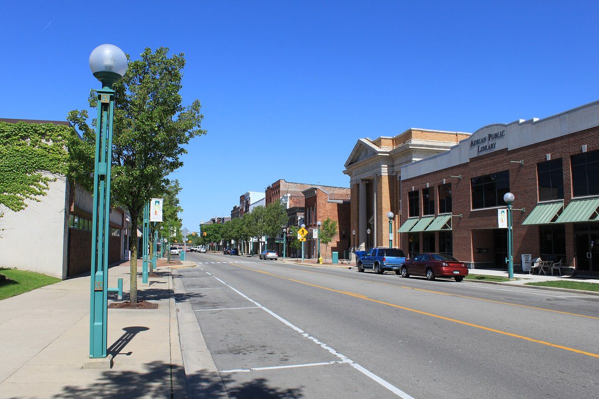 Maumee Street in downtown Adrian on a sunny day, with green lampposts, brick storefronts and the Adrian Public Library on the right