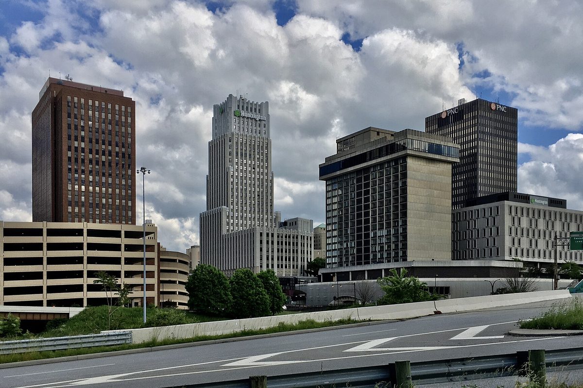 Downtown Akron towers, from the dark brown FirstEnergy Building to the PNC Center, rising behind a parking deck and a curving stretch of Martin Luther King Boulevard under heavy clouds