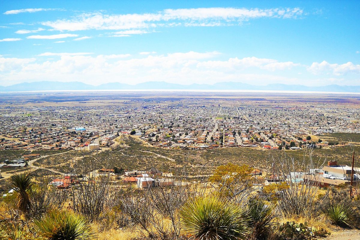 View over Alamogordo's streets from a desert hillside with yucca and dry scrub in front and distant mountains under a blue sky