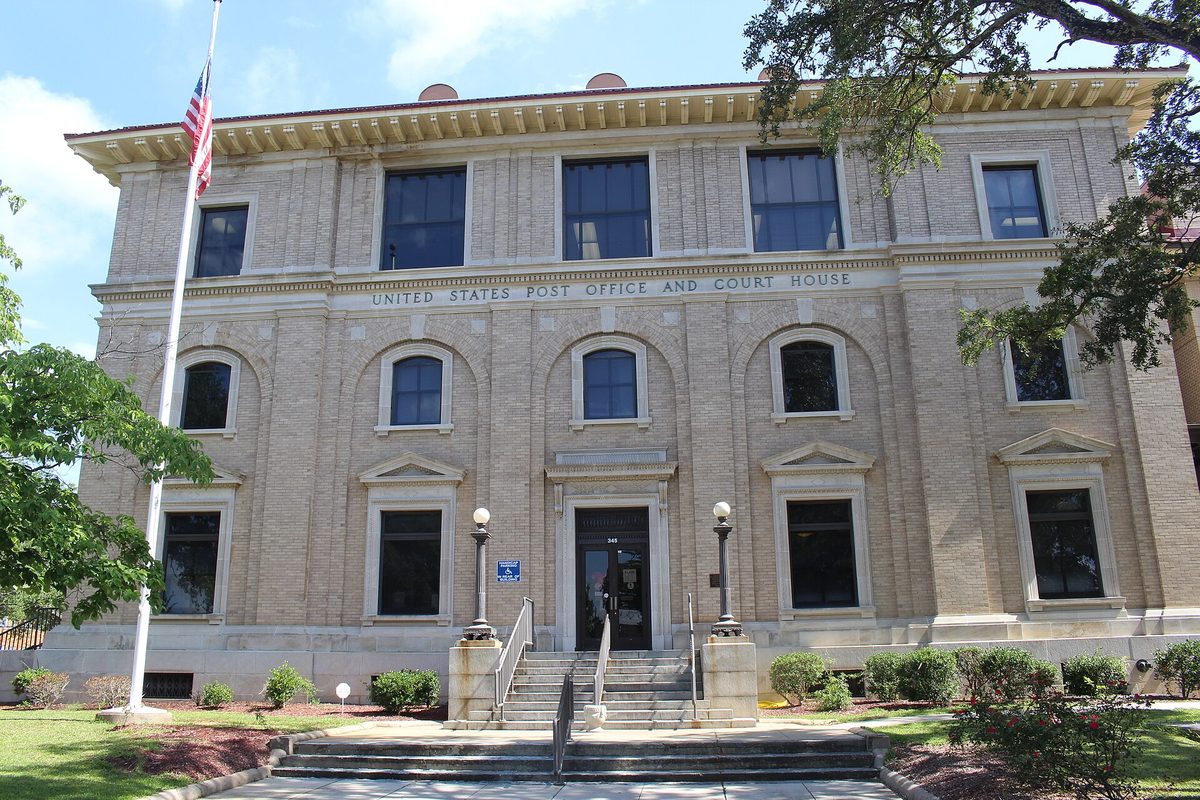 The tan brick U.S. Post Office and Court House in Albany, with arched windows, front steps and a flagpole, under a blue sky