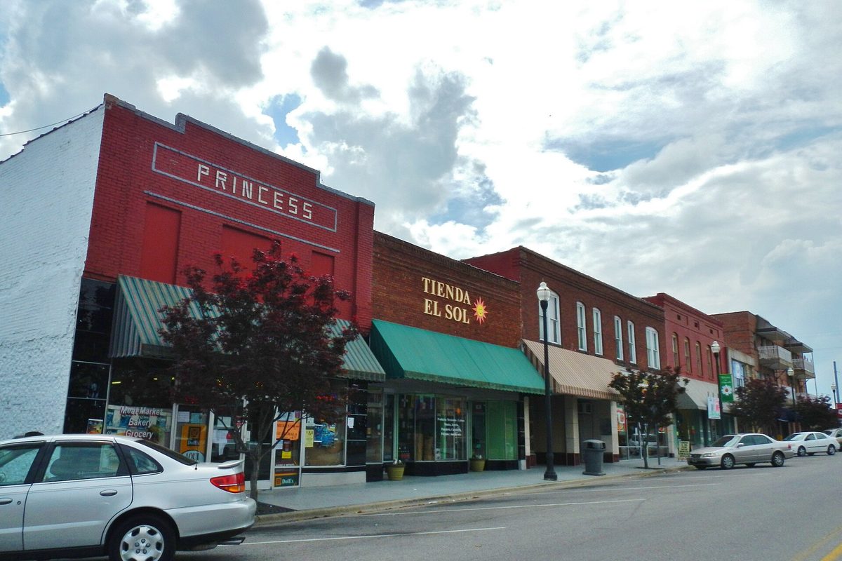 Red brick storefronts in downtown Albertville, including the old Princess building and a shop with a green awning, with a silver car parked at the curb