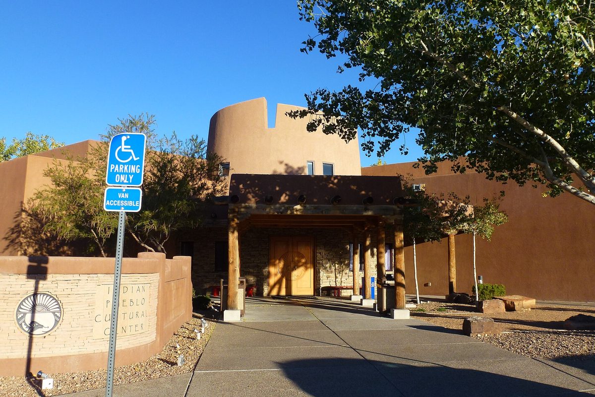 Adobe-style entrance of the Indian Pueblo Cultural Center in Albuquerque, with wooden doors, a round tower and an accessible-parking sign