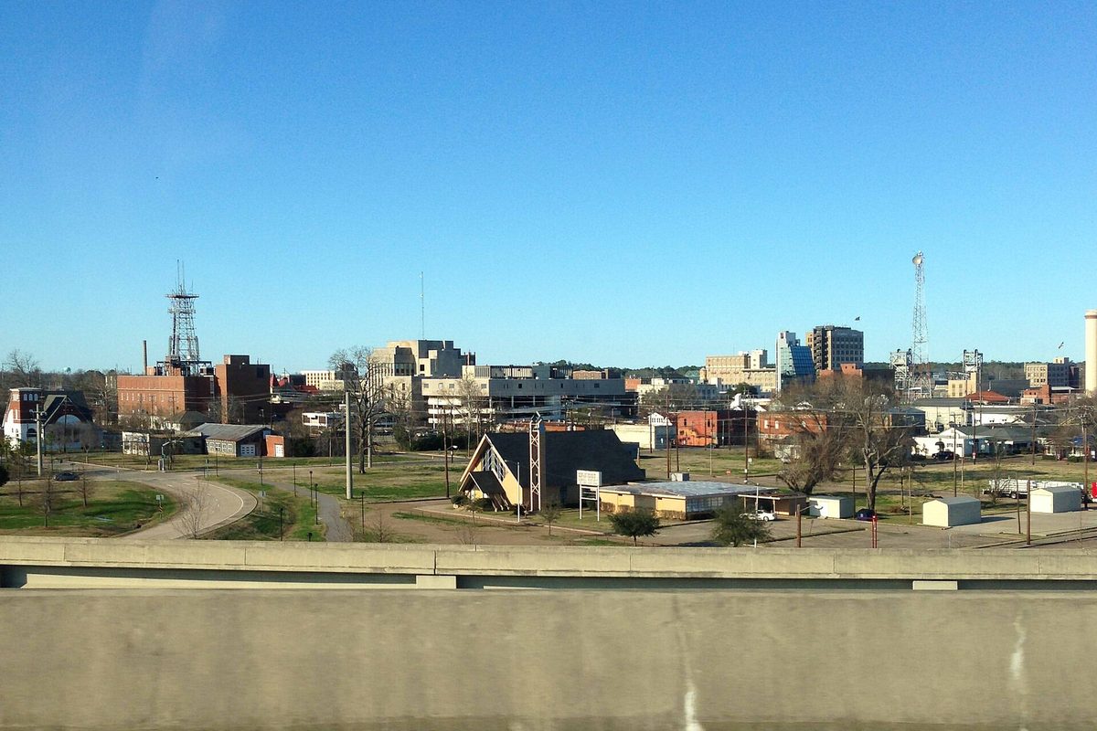 Downtown Alexandria's office towers and brick buildings under a clear blue sky, seen from a highway overpass