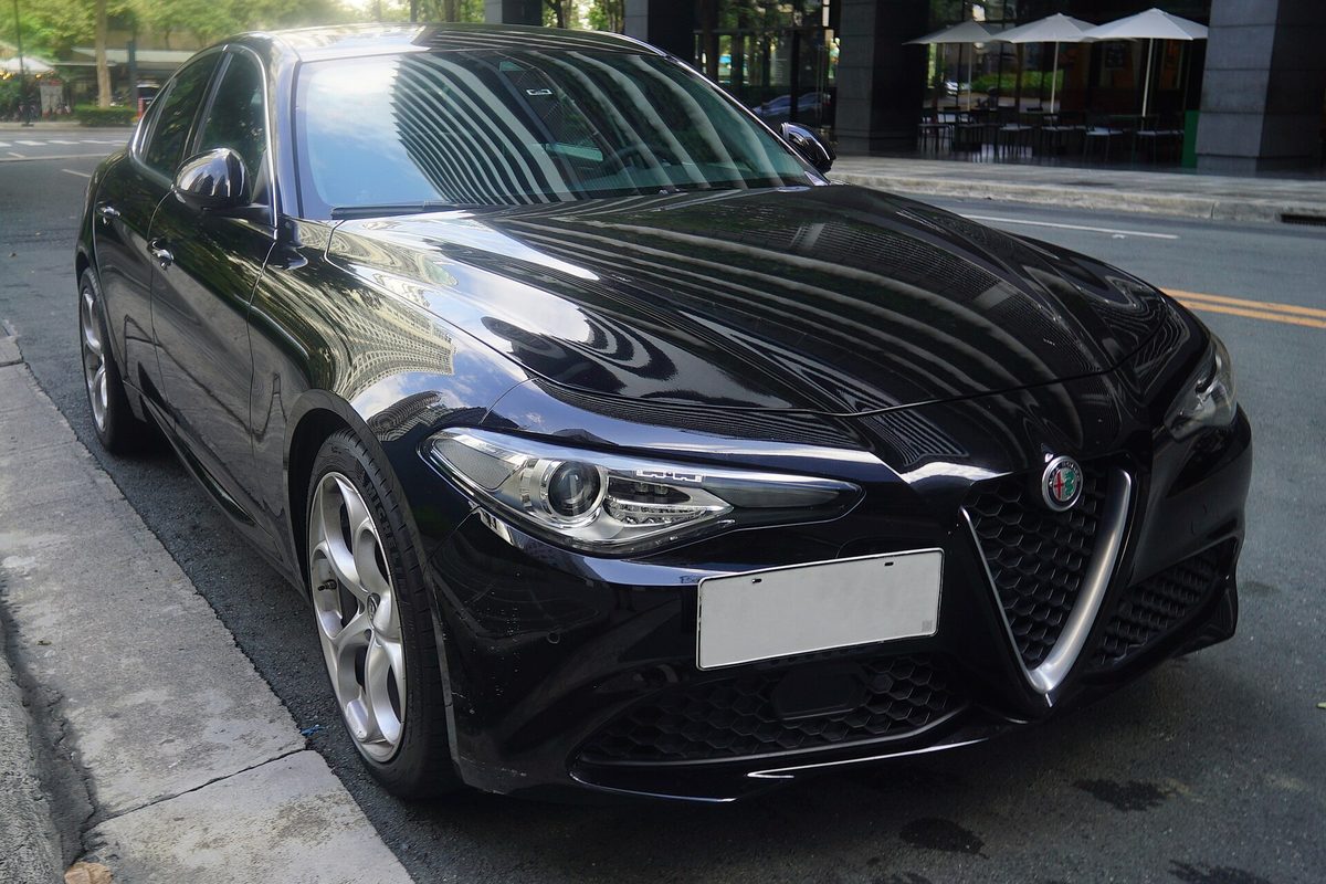 A black Alfa Romeo Giulia sedan with multi-spoke alloy wheels, parked at a city curb