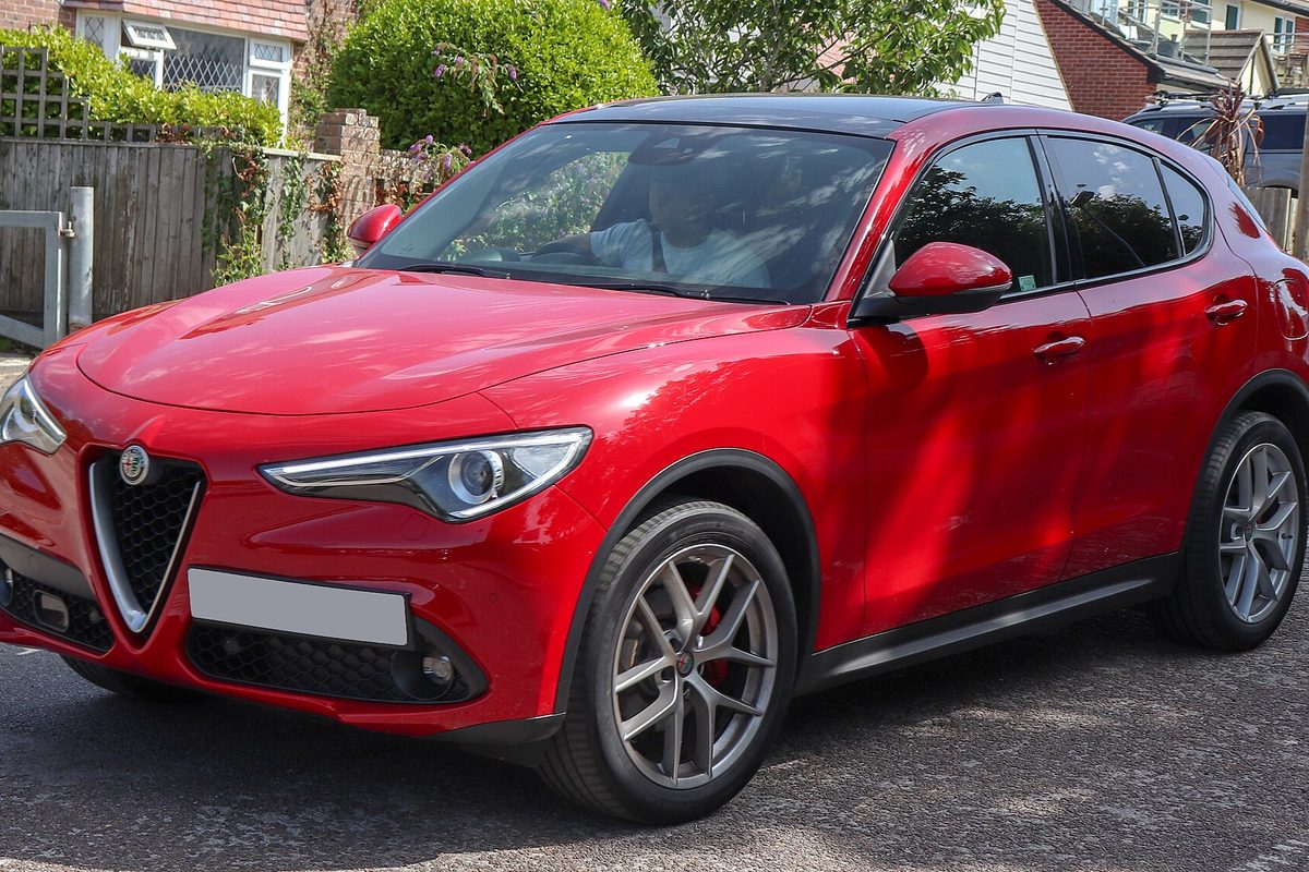 A red Alfa Romeo Stelvio SUV with silver alloy wheels and red brake calipers, parked on a residential street