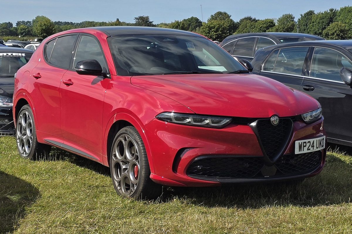 A red Alfa Romeo Tonale compact SUV with dark multi-spoke wheels, parked on grass at an outdoor car show
