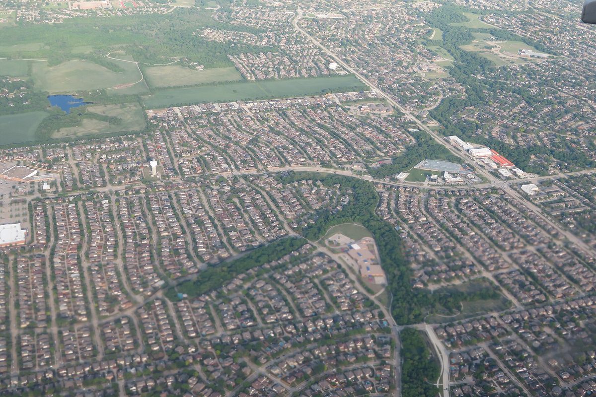 Aerial view of Allen, Texas: curving streets of rooftops, a wooded creek corridor, open fields and a small pond in the distance