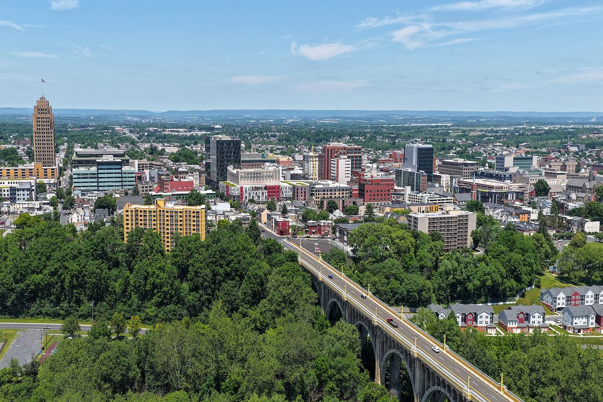 Aerial view of downtown Allentown with a tall stone tower at left, a long arched concrete bridge crossing a wooded valley, and hills on the horizon