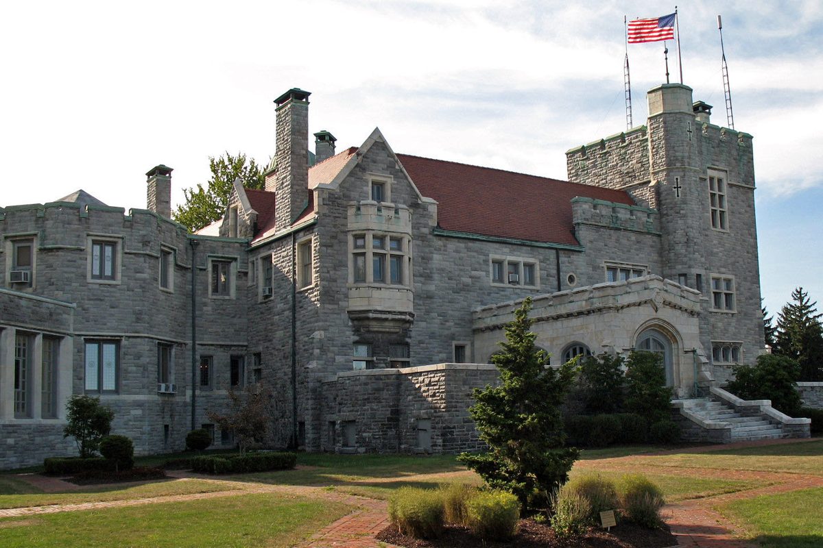 Glamorgan Castle in Alliance, a gray stone mansion with towers, bay windows and a red tile roof, behind a lawn, with an American flag flying above