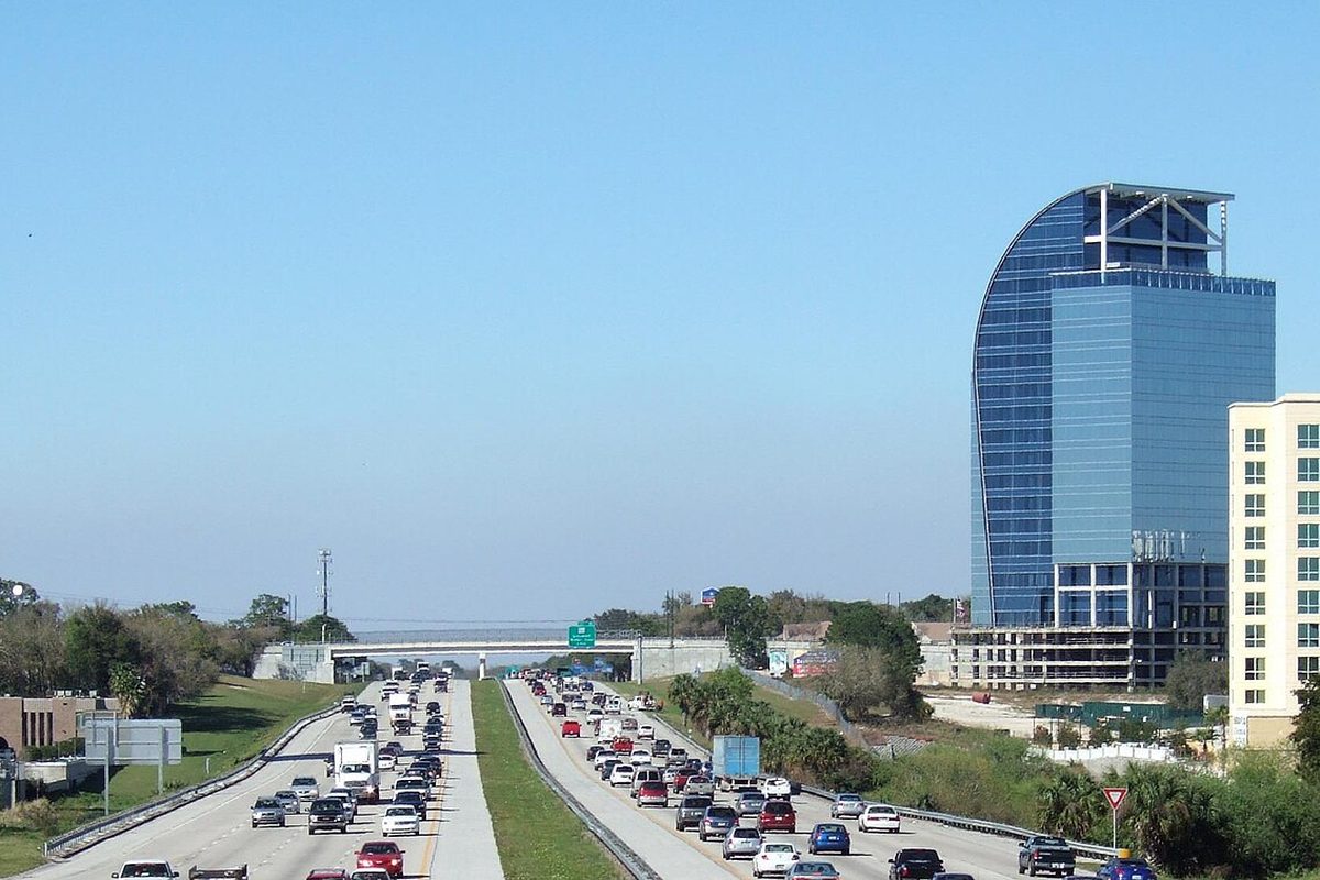 Traffic on Interstate 4 through Altamonte Springs, with a tall curved blue glass tower and an overpass under a clear sky
