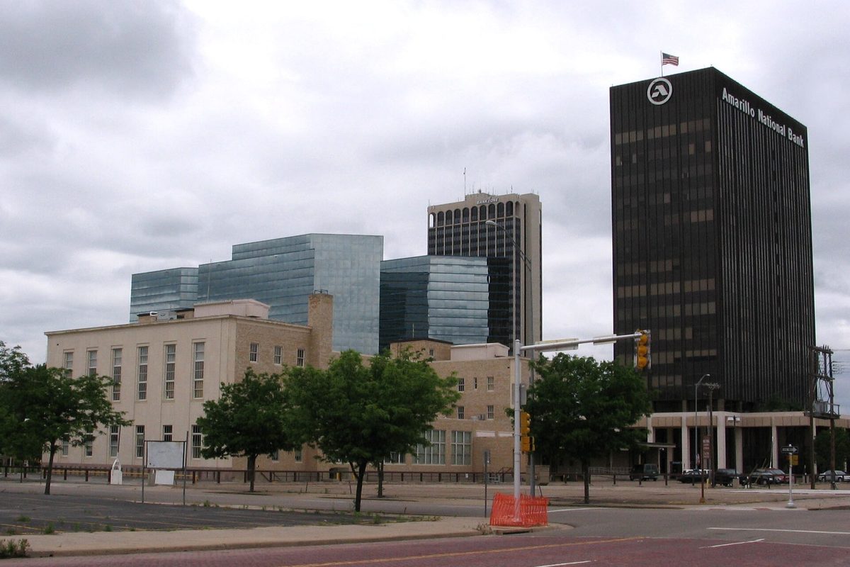 Downtown Amarillo under a gray, cloudy sky: the dark Amarillo National Bank tower on the right, a glass office building and a tan stone building behind green trees on the left