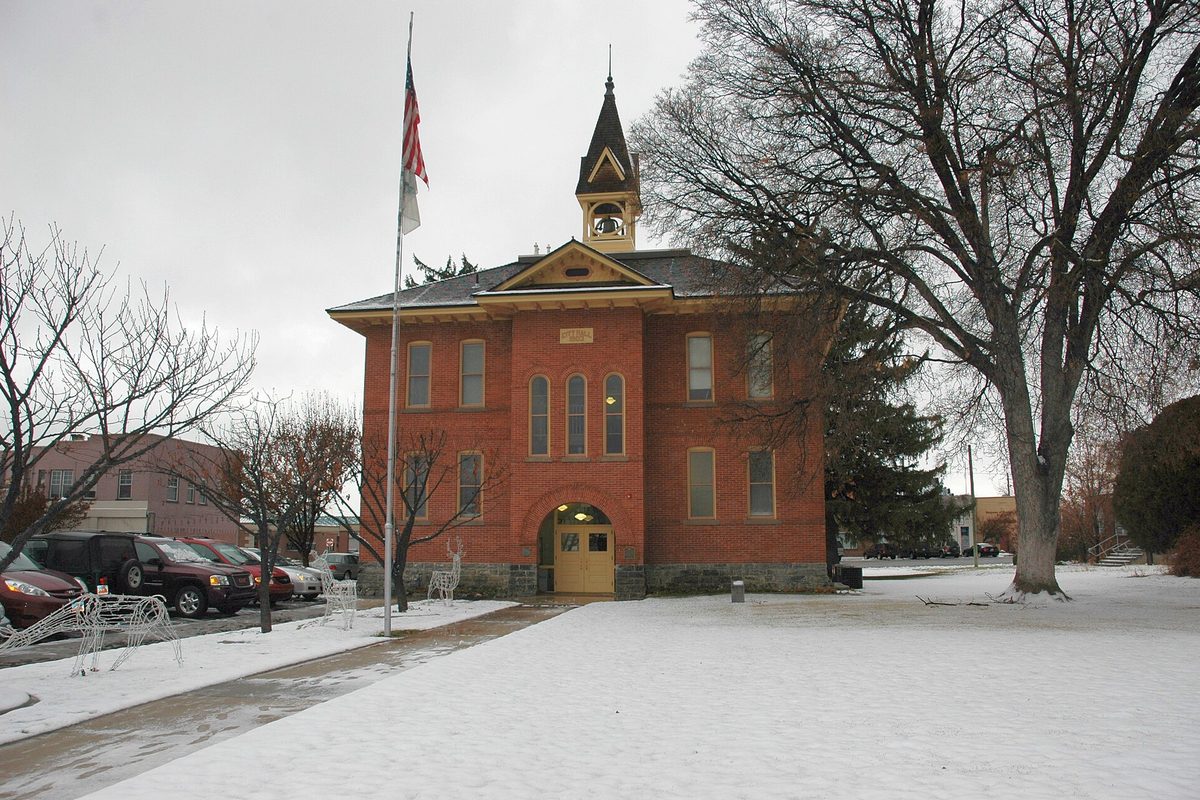American Fork's historic red-brick City Hall with a white bell tower, bare trees and a flagpole, on a snowy winter day