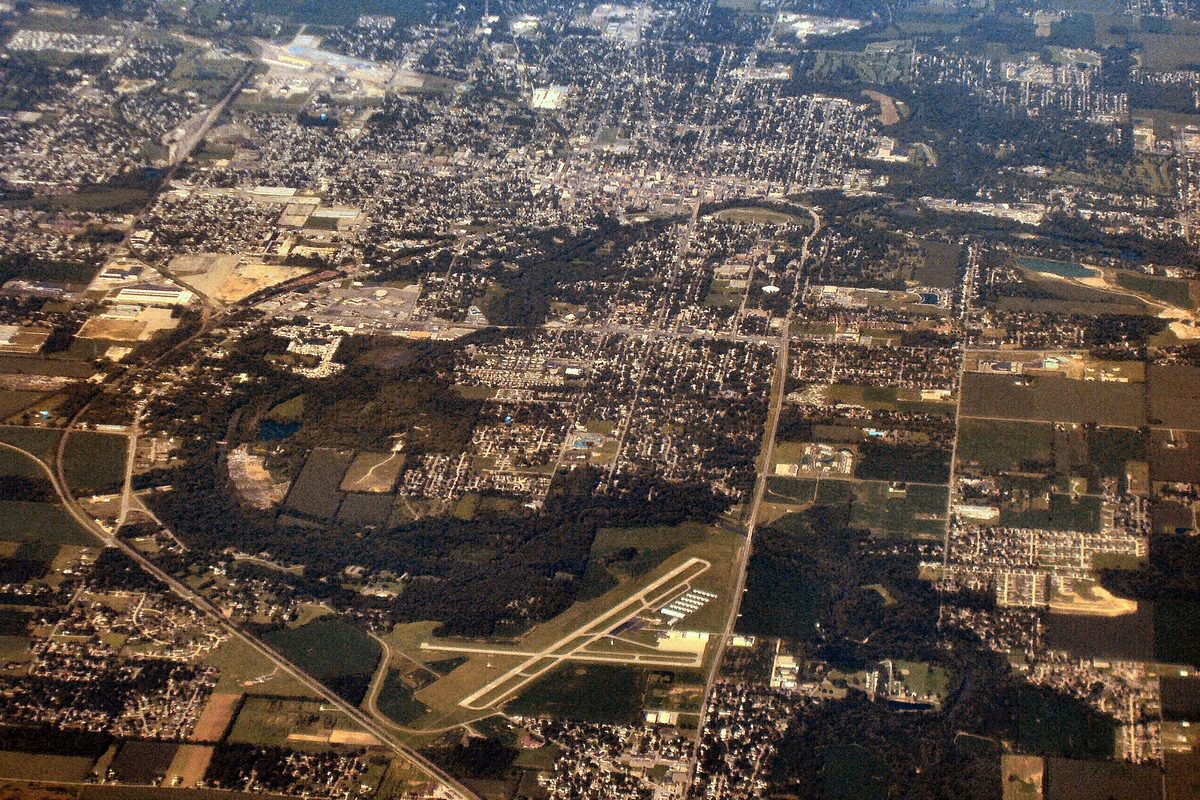 Aerial view of Anderson's street grid and neighborhoods, with an airport's crossing runways and farm fields in the foreground