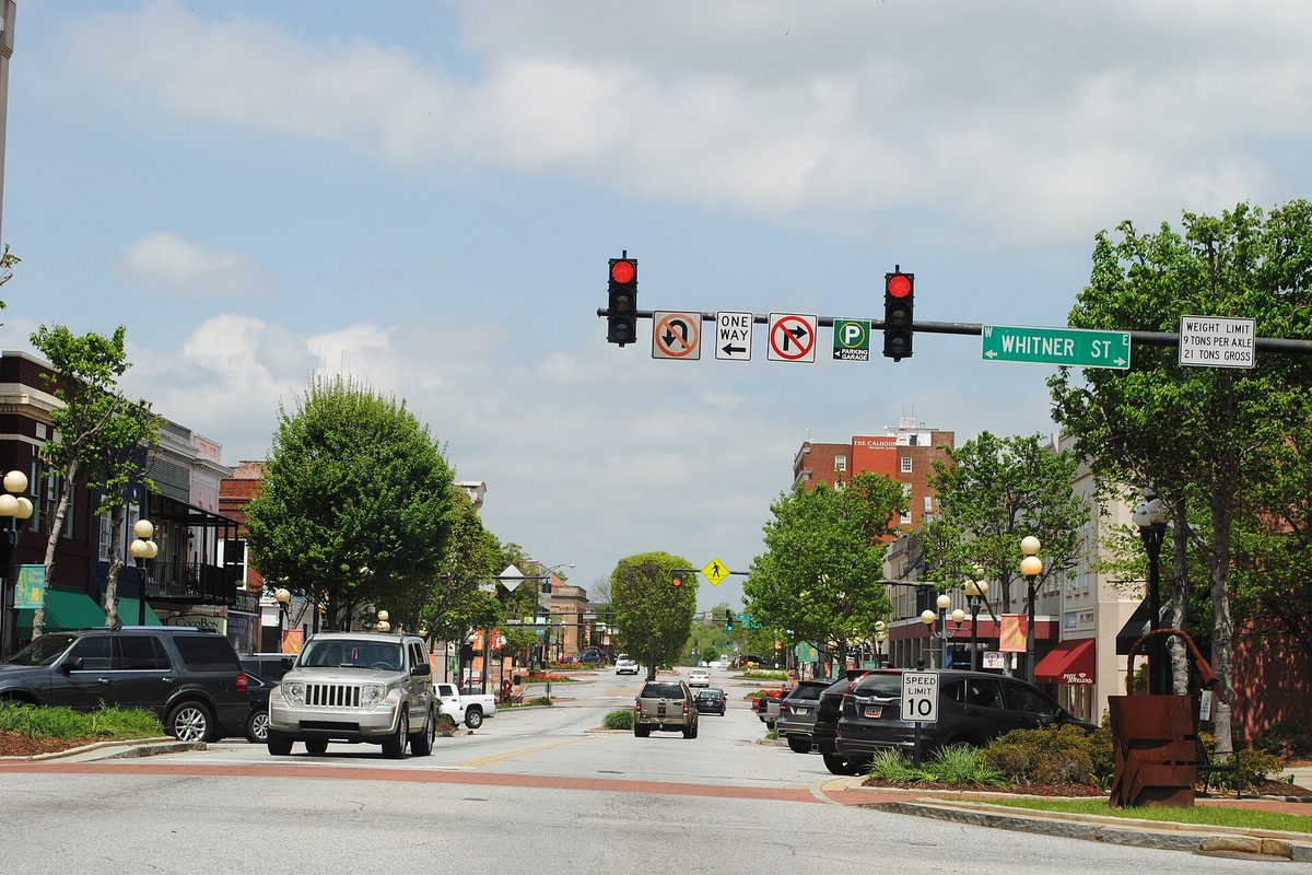 Main Street in downtown Anderson at the Whitner Street corner, with red traffic lights, trees and parked cars along brick storefronts