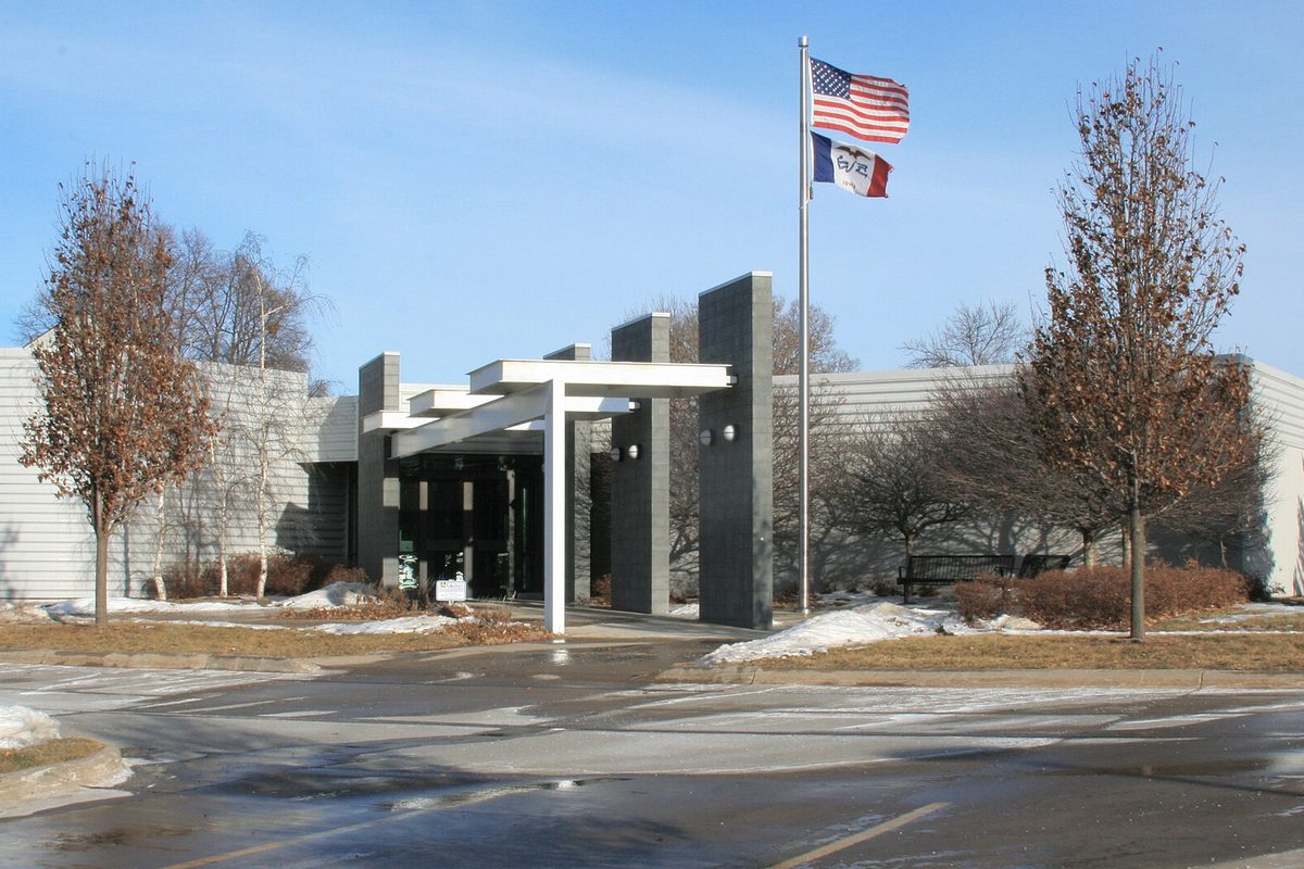Ankeny City Hall, a low gray building with a white pergola over the entrance and the U.S. and Iowa flags on a pole, with patches of snow on the lawn