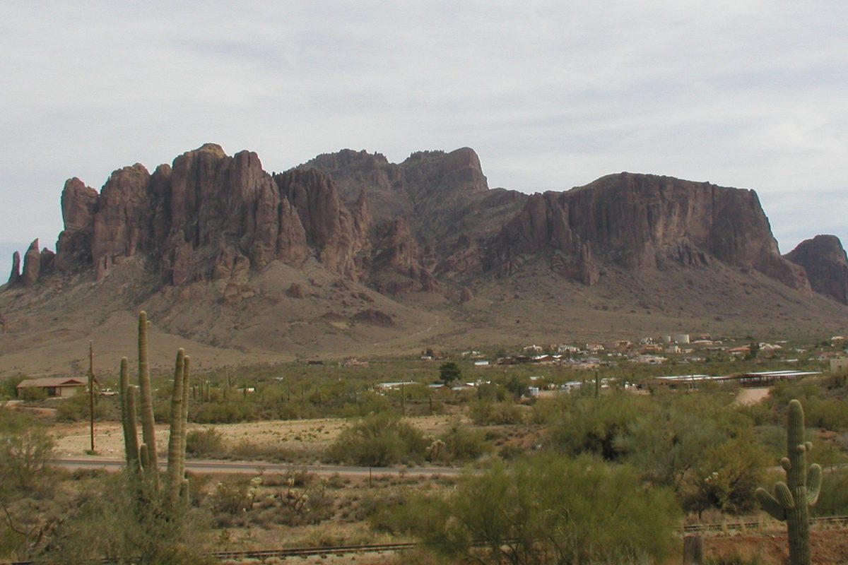 The jagged rock face of Superstition Mountain above desert scrub, saguaro cactus and scattered homes in Apache Junction