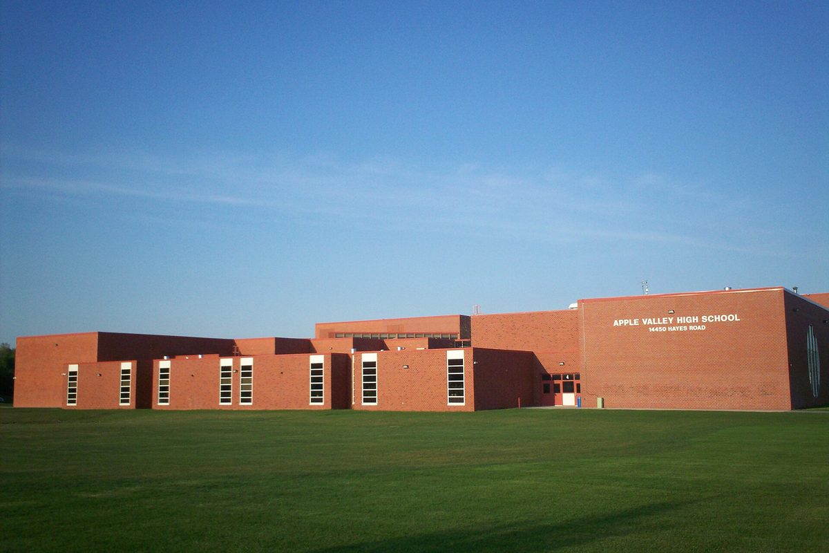 The long red-brick west side of Apple Valley High School, its name and Hayes Road address lettered on the wall, behind a wide green lawn under a blue sky