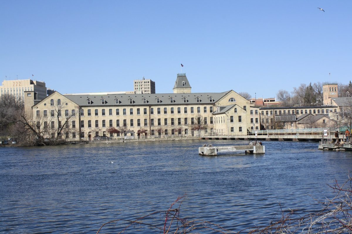The long cream-colored Fox River Paper Company mill buildings, now apartments, across the Fox River in Appleton under a clear blue sky