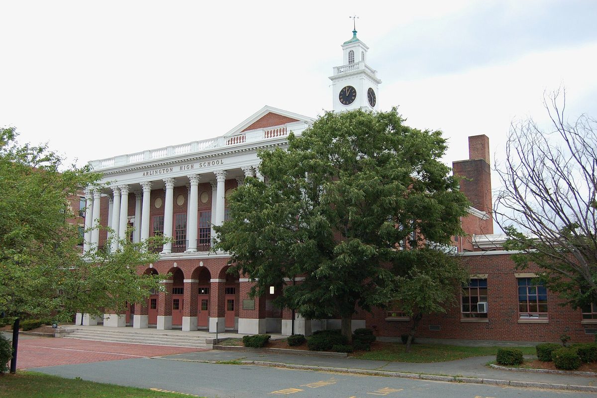 Arlington High School's brick front with white columns and a white clock tower, half hidden behind a large leafy tree