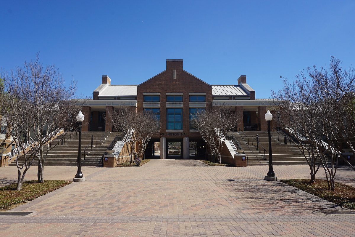 Arlington Hall at the University of Texas at Arlington, a red brick building with wide stairs on both sides, a brick plaza, lamp posts and bare trees