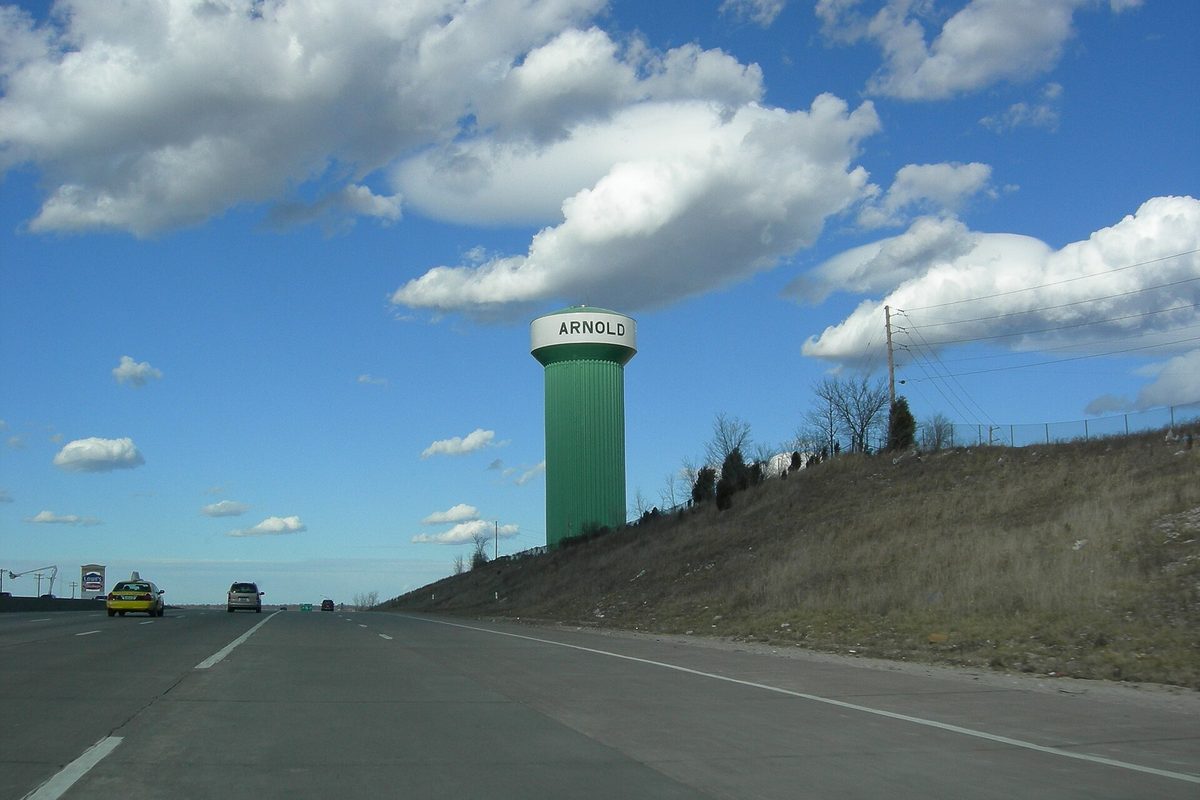 Arnold's green water tower, its white top lettered ARNOLD, above a grassy slope beside I-55 with cars on the highway