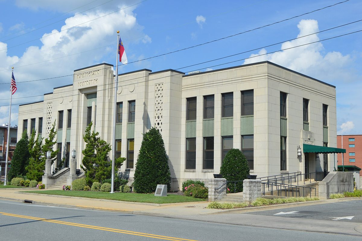 Asheboro's pale stone municipal building on North Church Street, with tall windows, a green entrance awning and the U.S. and North Carolina flags out front