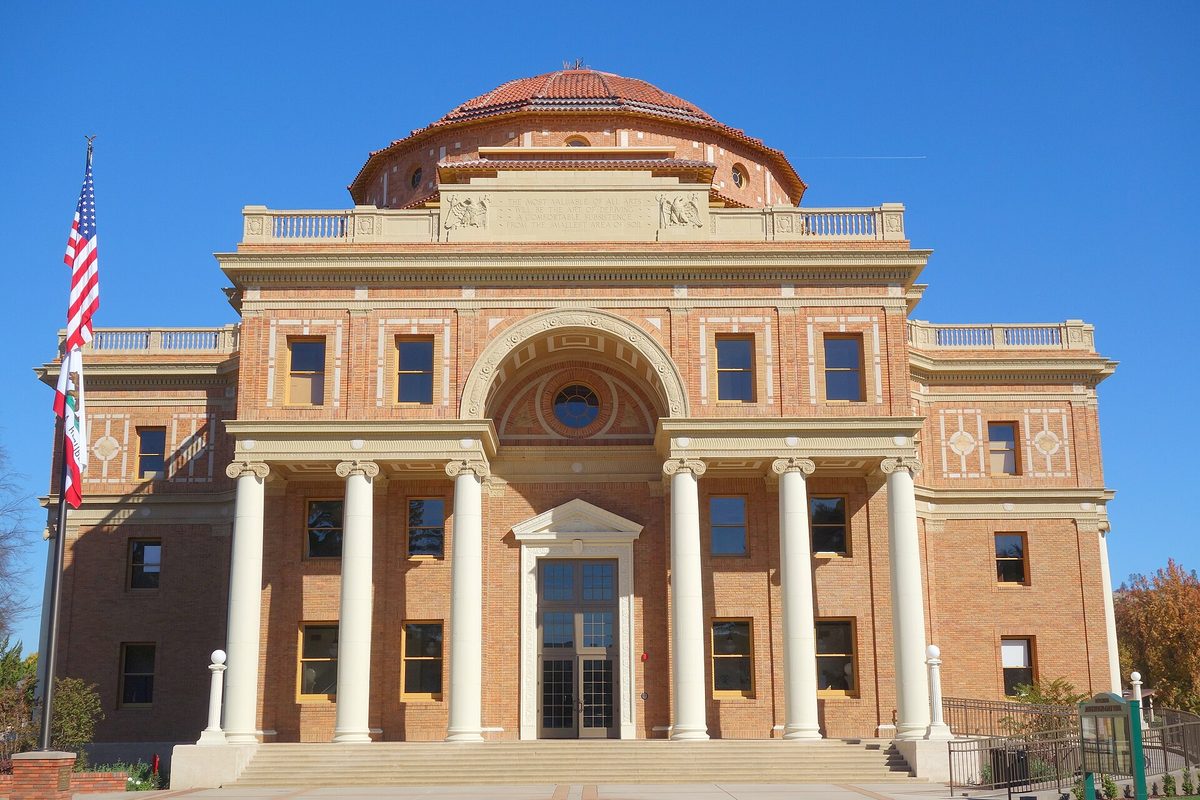 Atascadero City Hall, a domed brick building with tall white columns and an arched entrance, under a clear blue sky with a US flag