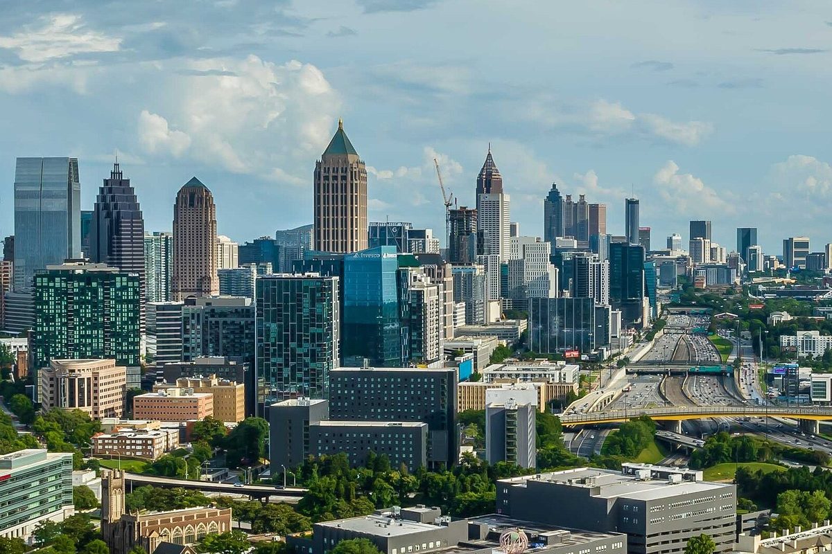 Midtown and Downtown Atlanta towers under a cloudy blue sky, with a busy interstate curving past the skyline on the right