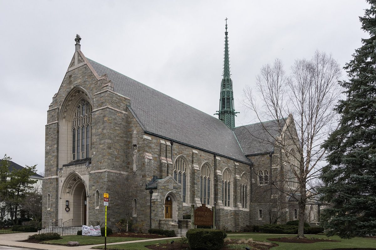 The gray stone St. John the Evangelist church in Attleboro, with a pointed arched entrance, tall stained-glass windows and a green copper spire