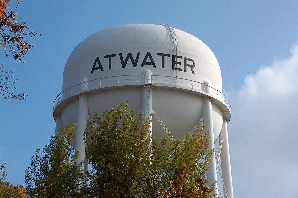 Atwater's white water tower, the town name painted across the tank in dark letters, rising above autumn trees against a blue sky