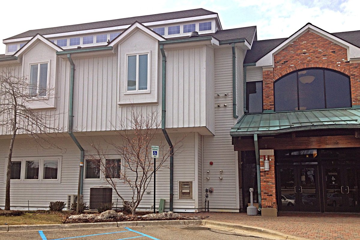 The north entrance of Auburn Hills City Hall: white siding beside a brick and glass entry under a green metal awning
