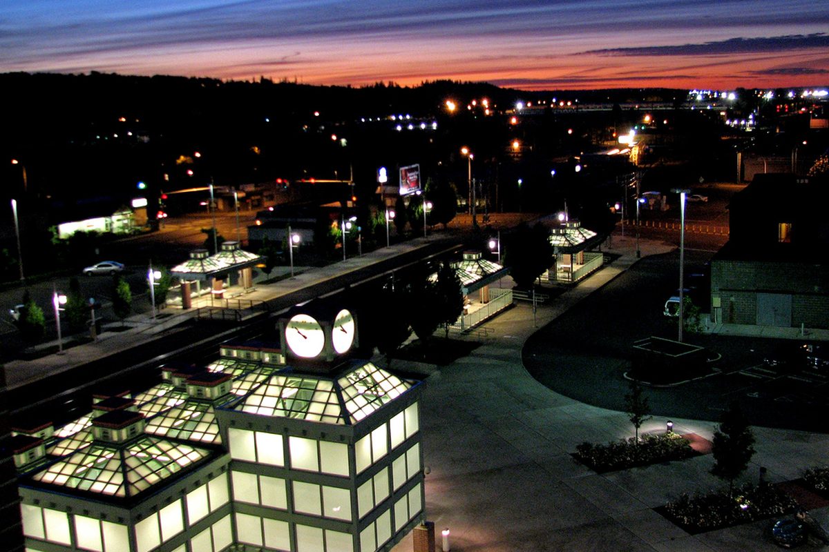 Auburn's train station at dusk, its glass-roofed shelters and a two-faced clock lit up under an orange and purple sky