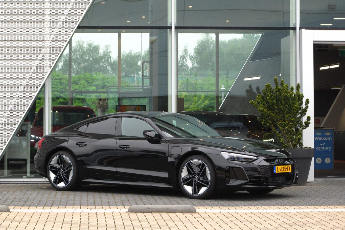 A black Audi e-tron GT four-door with black and silver wheels, parked in front of a glass-walled dealership