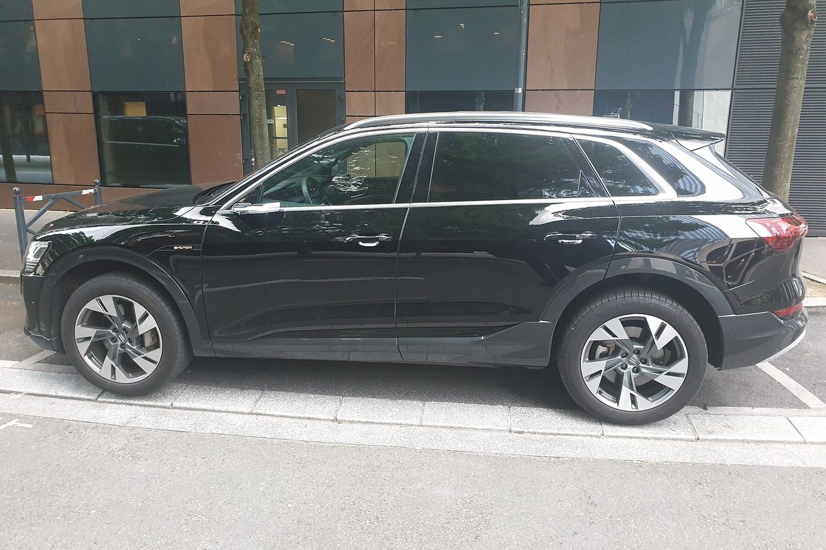A black Audi e-tron SUV seen from the side, parked along a city sidewalk