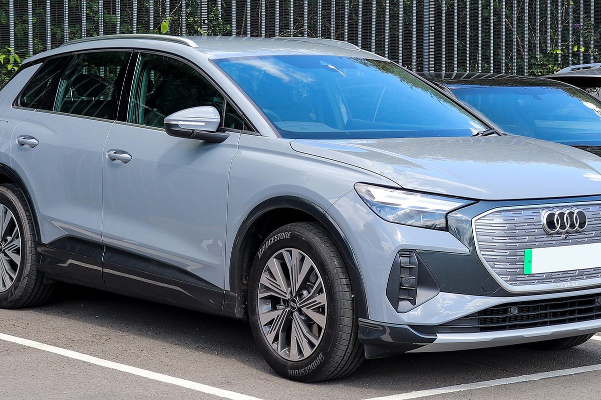 A pale gray Audi Q4 e-tron SUV in a parking bay in front of a tall metal fence