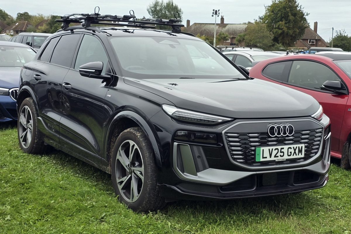 A black Audi Q6 e-tron SUV with roof bars, parked on grass among other cars