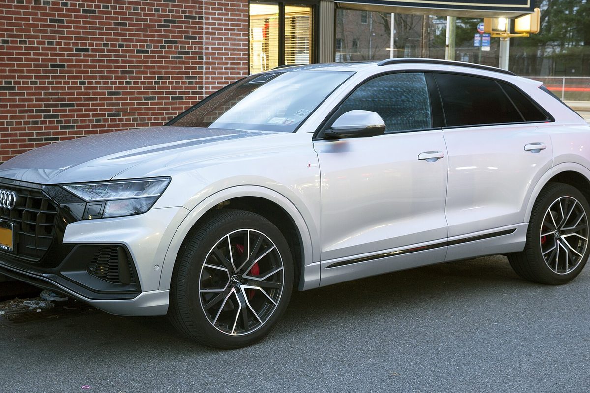 A silver Audi Q8 with black and silver wheels parked in front of a brick building
