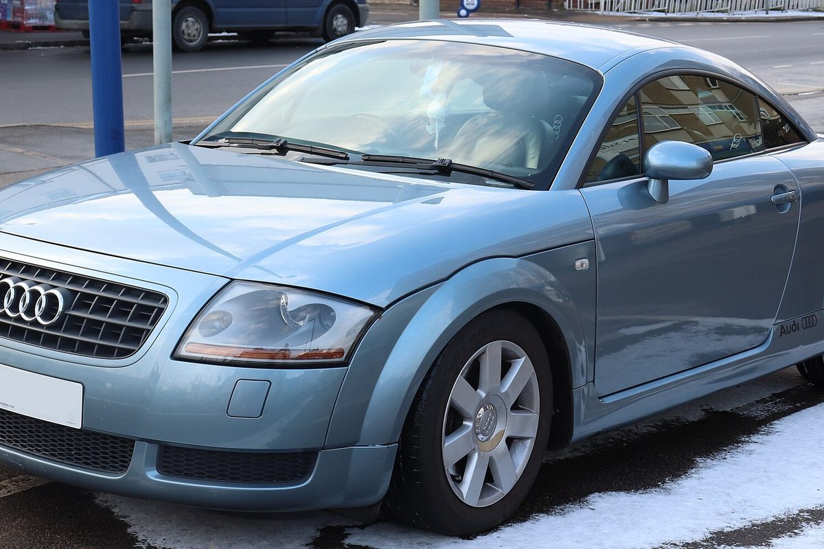 A pale blue first-generation Audi TT coupe parked at a curb with patches of snow on the ground