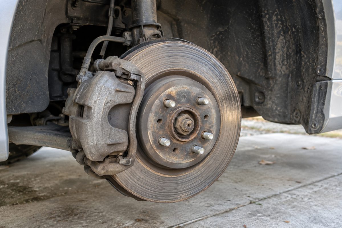 A car's front wheel hub with the wheel off, showing a rust-streaked brake rotor and a grimy caliper above a concrete floor
