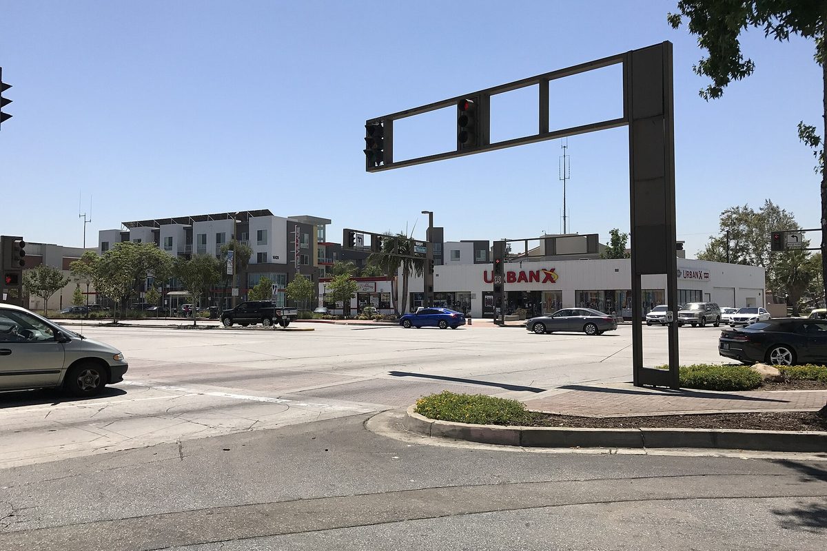 A wide Baldwin Park intersection with traffic signals, cars waiting at the light, a store and a newer apartment block under a clear sky