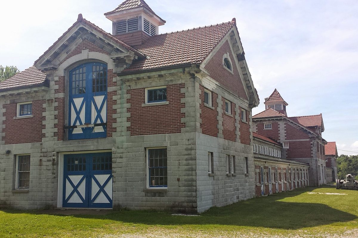 The O. C. Barber Piggery in Barberton, a long brick and stone farm building with blue and white barn doors and red tile roofs, on a mowed lawn