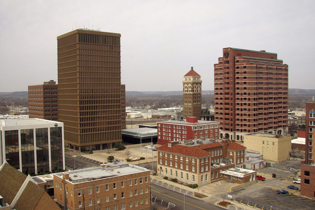Downtown Bartlesville from above on a gray day, with a brown high-rise, a red-brick tower block, a brick clock tower with a red roof and older brick buildings below
