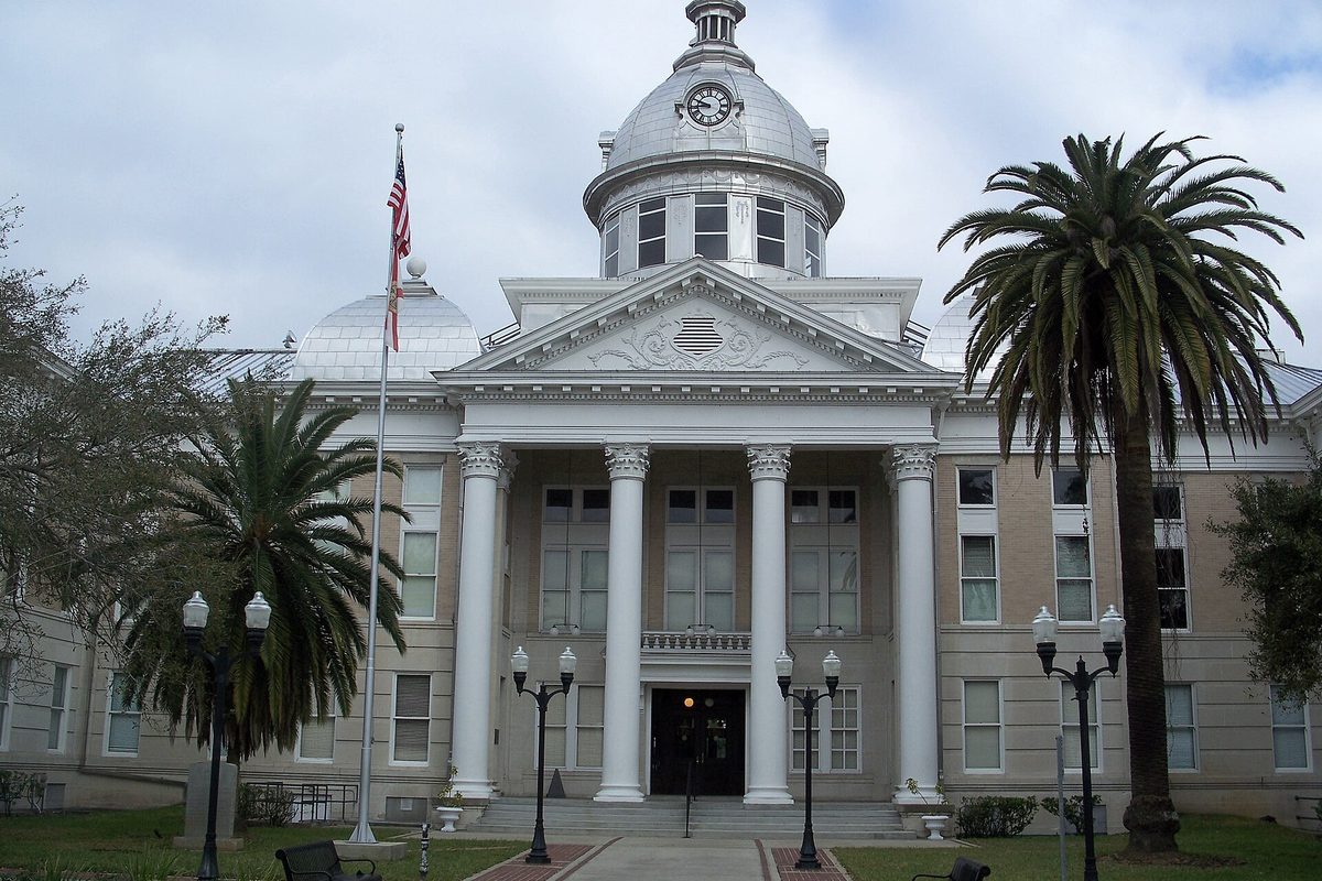 The old Polk County Courthouse in Bartow, a domed neoclassical building with tall white columns, a clock in the cupola, palm trees and an American flag